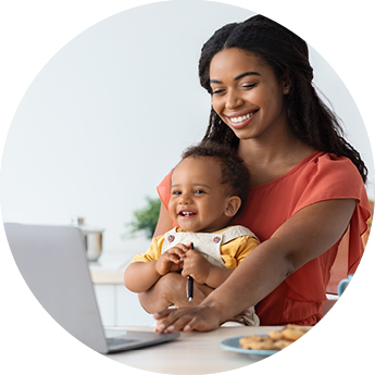 women with a baby in her hand whilst working on a laptop